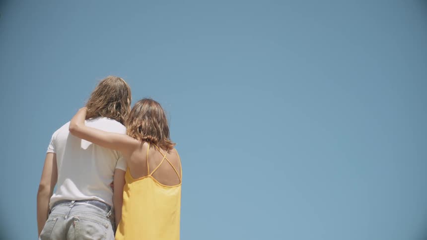 A woman hugs a man on a windy sunny day
