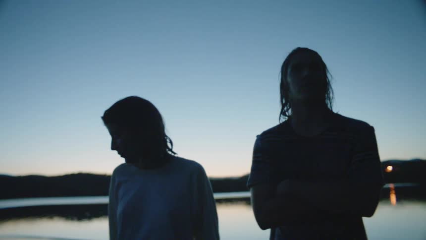 A man and woman stand on shore at sunset