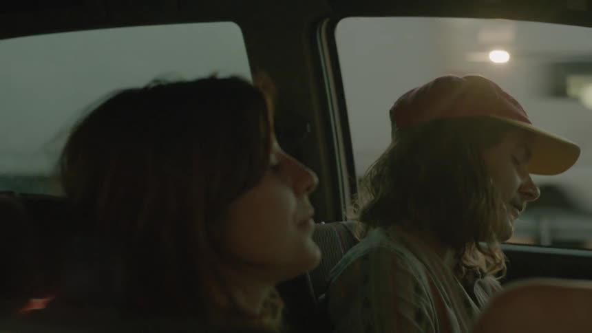 A man and woman sit in a parked car at sunset