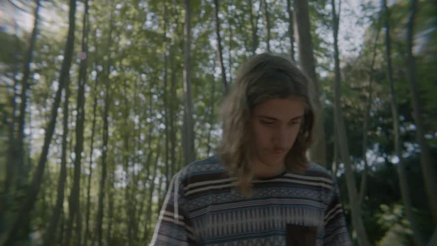 A teenage boy is pacing outside in a forest on a sunny day