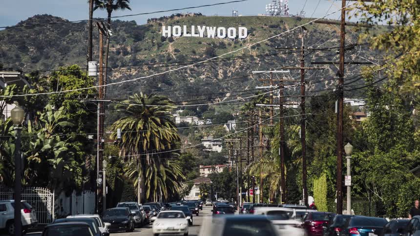 The hollywood sign overlooks traffic and pedestrians on a street