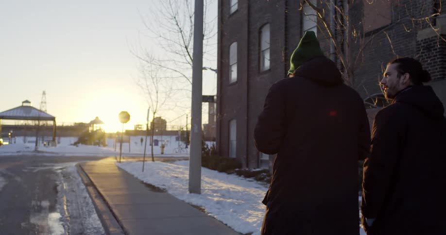 Two men are walking down the street talking in with snow on the ground