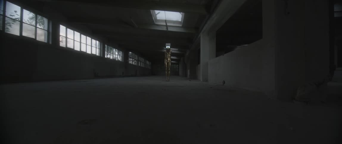 A dim empty warehouse with a screen flickering across the room