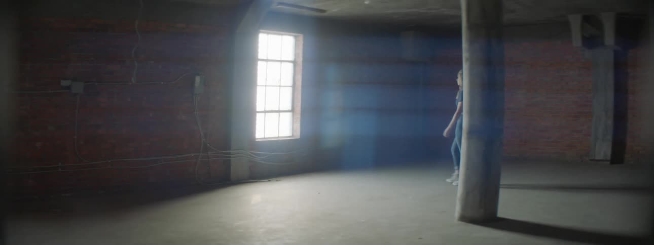 A woman walks to the window of an empty warehouse