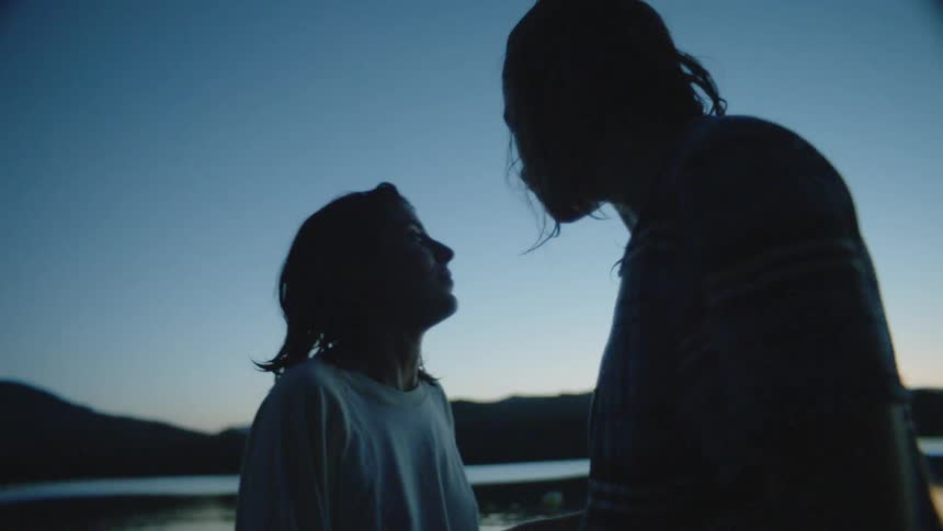 A man hugs his girlfriend as they stand on shore at sunset