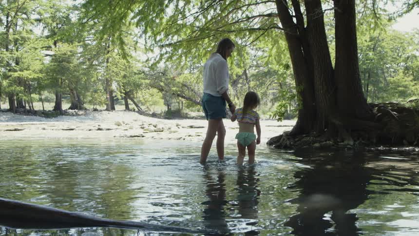 A mother and her daughter are wading across a river in daylight