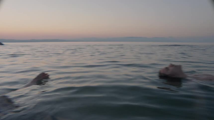 People are floating in the water at sunset