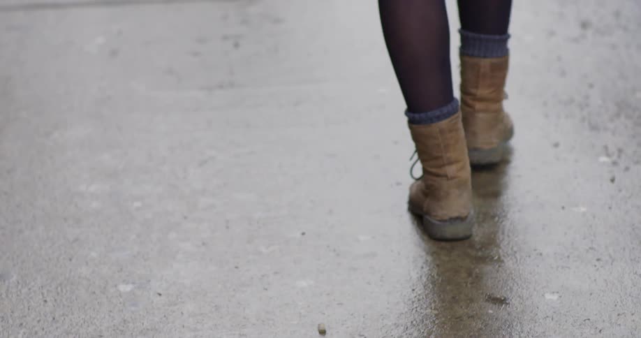 Person's legs walking on a sidewalk on a rainy day