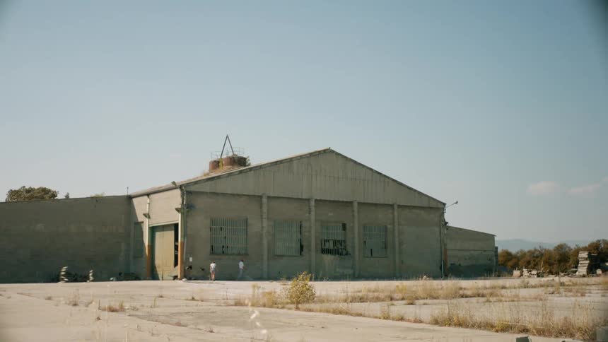 Two people walk up to an abandoned building with broken windows