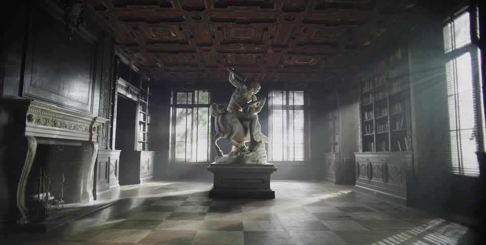 Sun shines through the windows of a room with bookshelves and a large statue