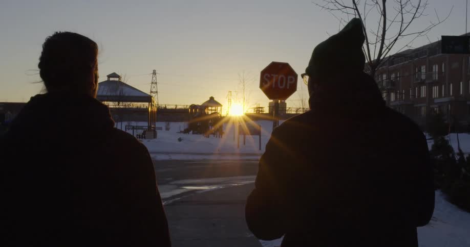 Two men walking down a road towards a stop sign