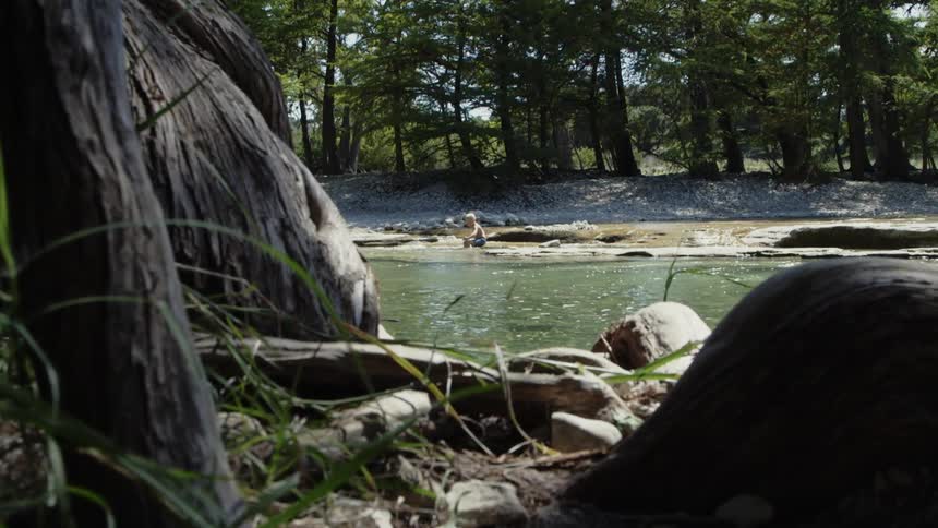 A kid is sitting on the edge of a small creek