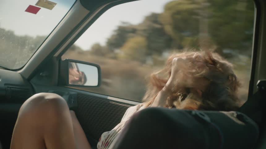 Woman leans her head on open window of a moving vehicle