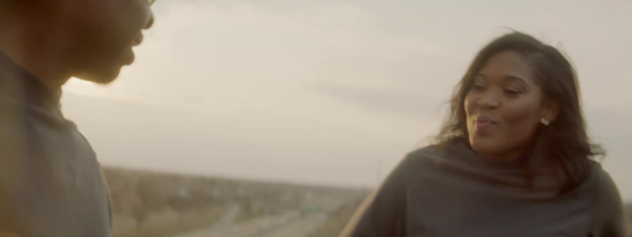 Smiling man and woman talk on a rooftop with a highway below