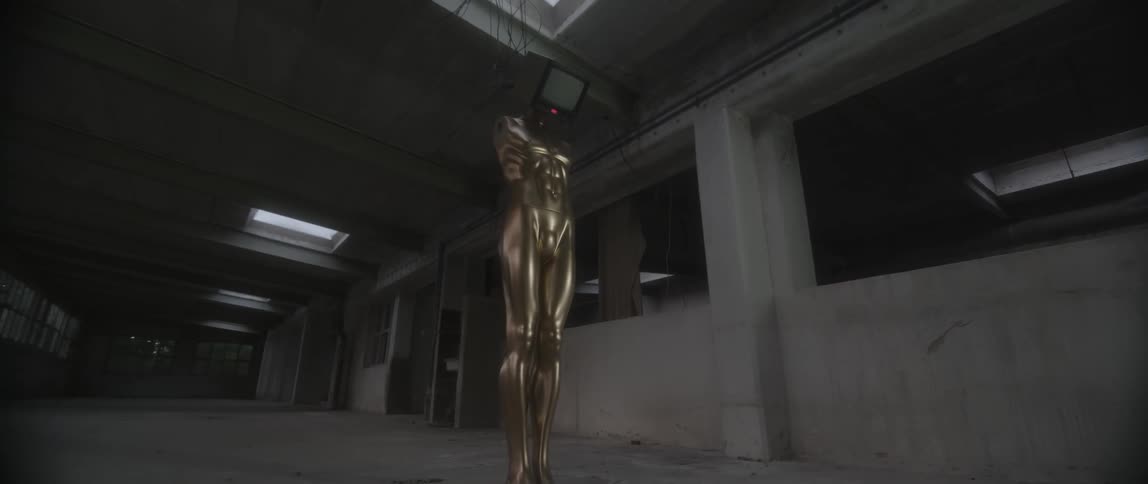 Gold colored statue with a monitor on top stands in a large building