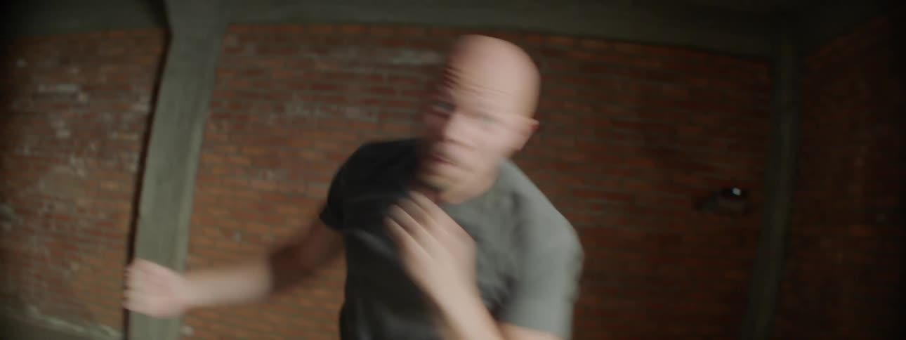 Bald man practices boxing jabs in a large room
