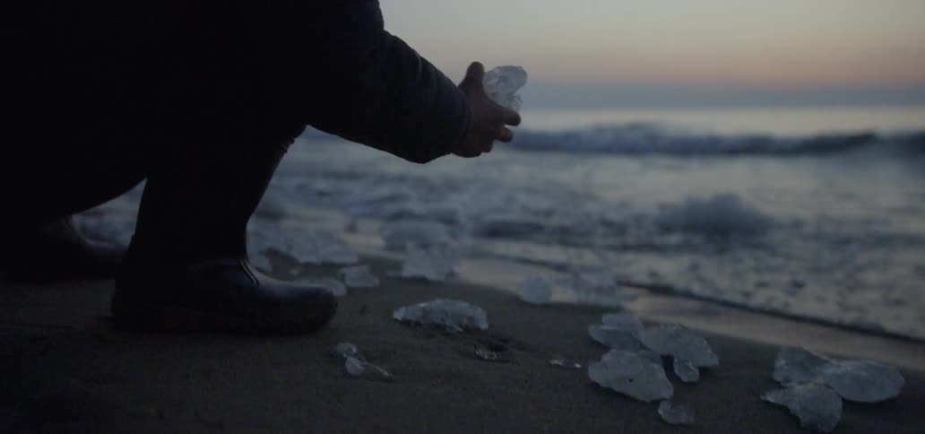 A boy picks up a chunk of ice on the beach