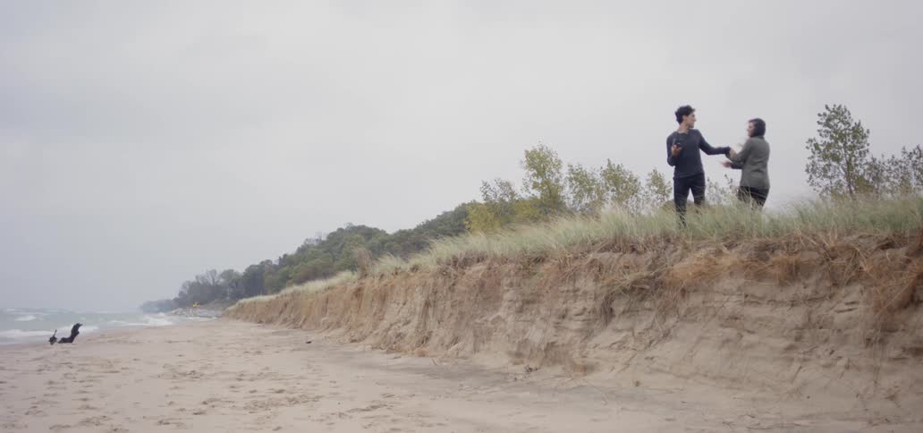 Man and woman stand on a hill as they look out at the water