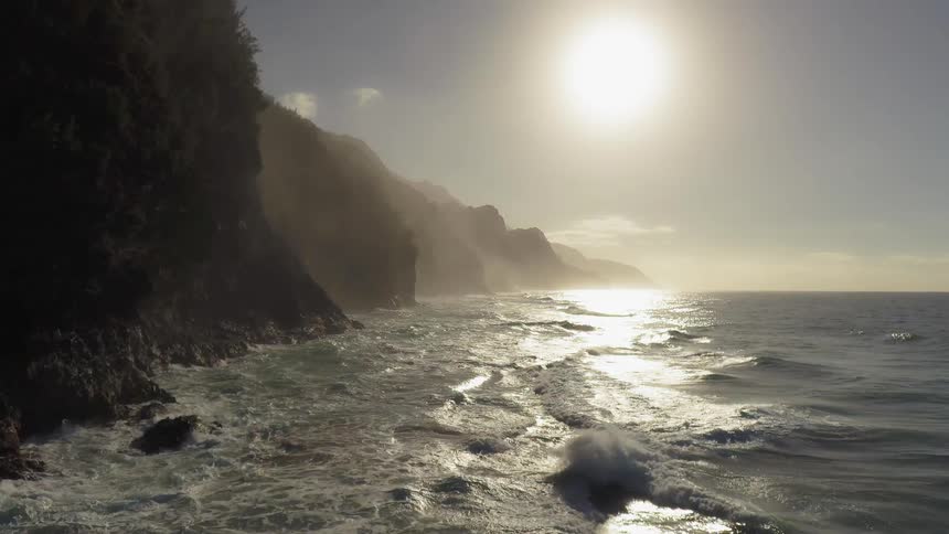 Frothy waves roll towards hills under the bright sun