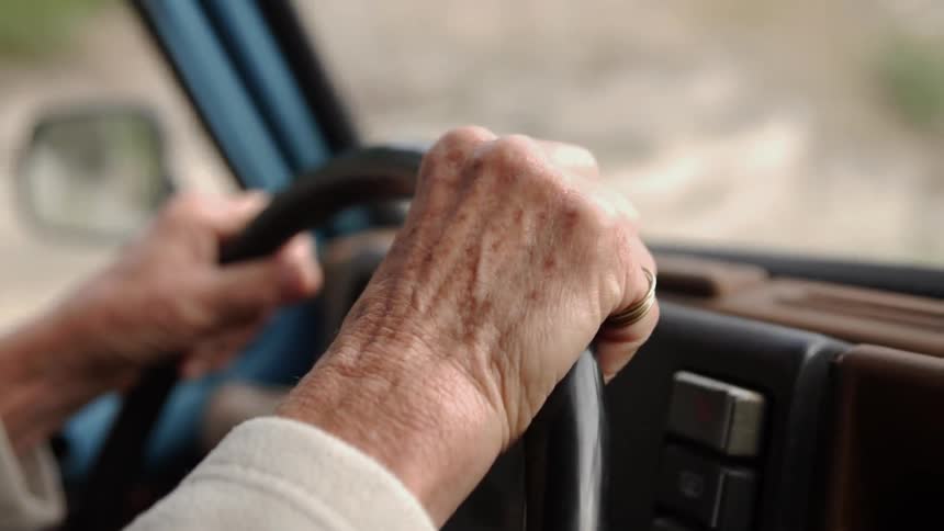 Elderly person grips a steering wheel of a car