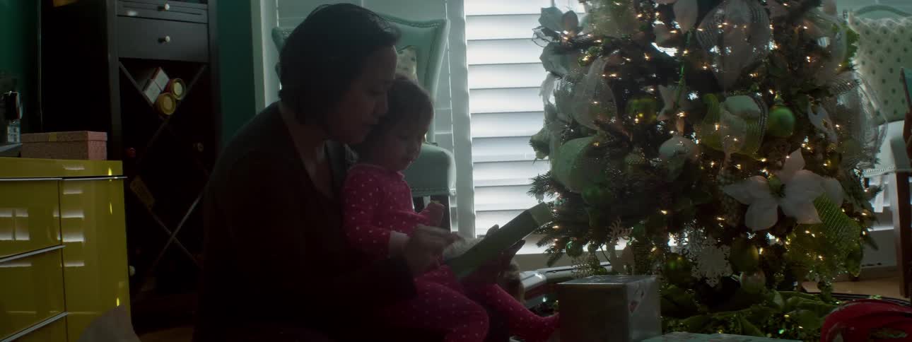 A woman and child look at a toy near the christmas tree