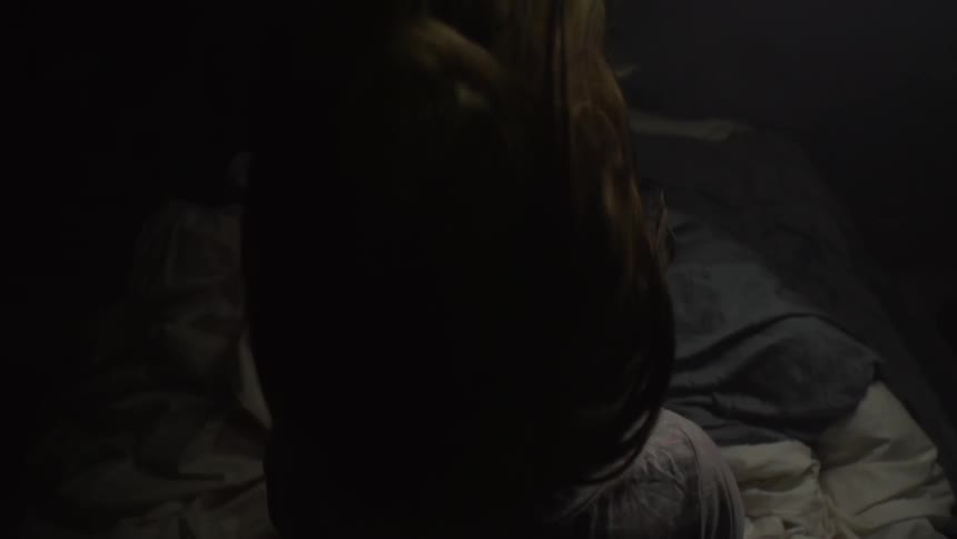A woman on a bed shakes her hair in slow motion in dark room