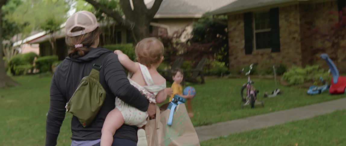 A woman carries a child towards the home