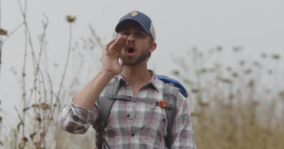 A man wearing a backpack is walking down a trail and turns to yell at someone