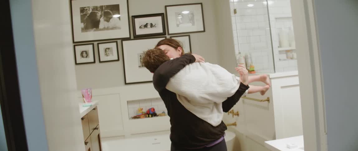 A mom wraps up her child in a towel and carries him out of the bathroom
