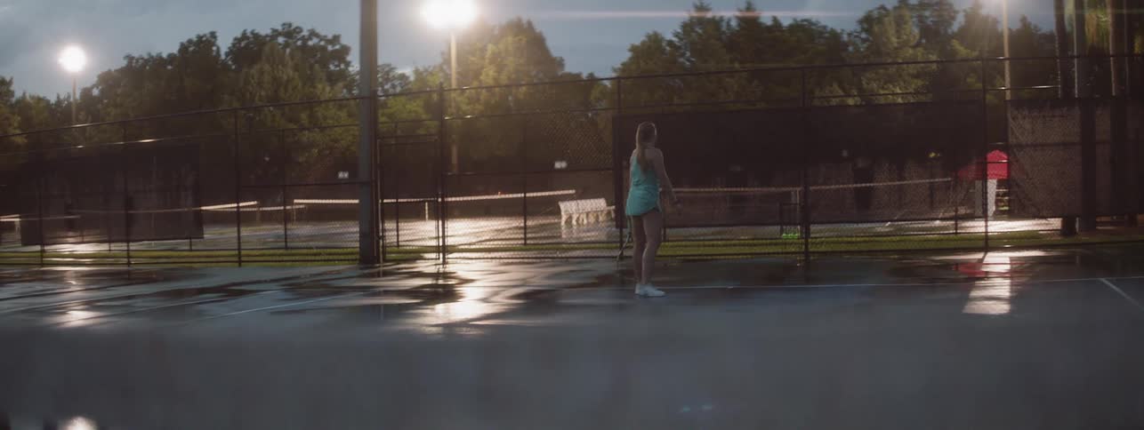 Woman plays tennis on a court at night