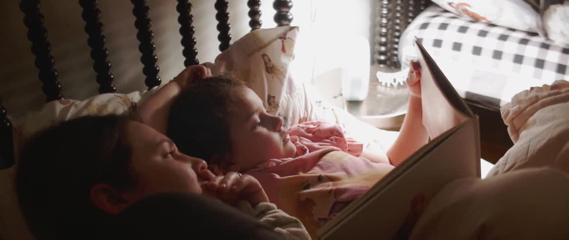 Woman and child lay in bed reading a book