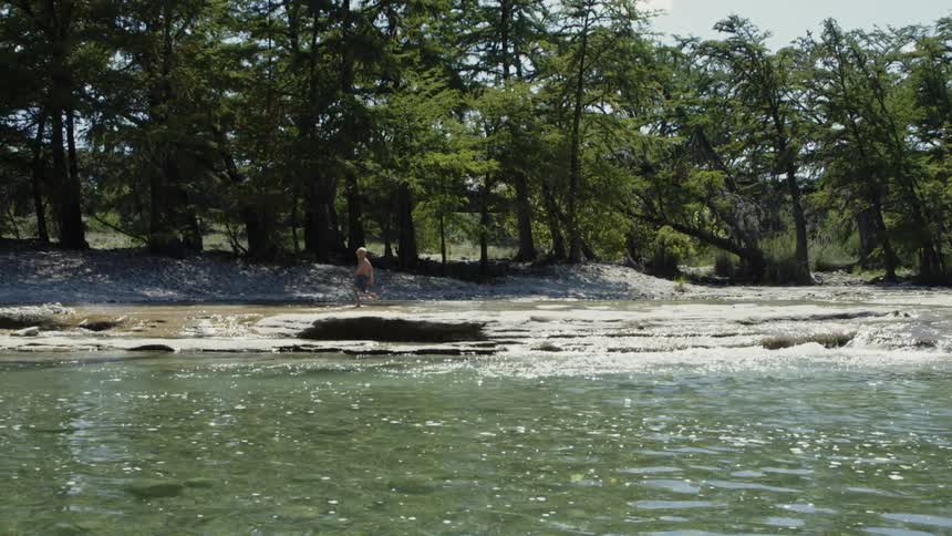 A boy walks next to a river in a swimsuit