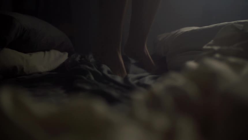 Feet jump off bed in slow motion in dark room
