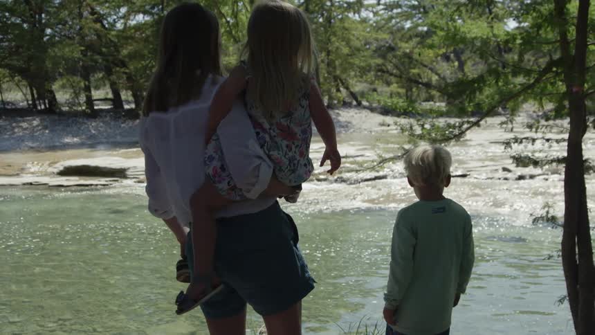 A woman and young children stand next to a river