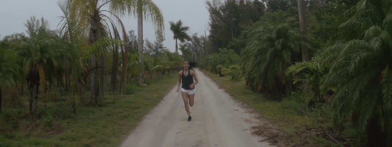 A woman runs down a dirt path lined with trees