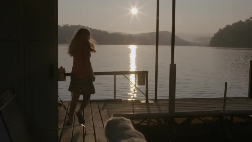 A girl and dog running along a wooden deck near a lake