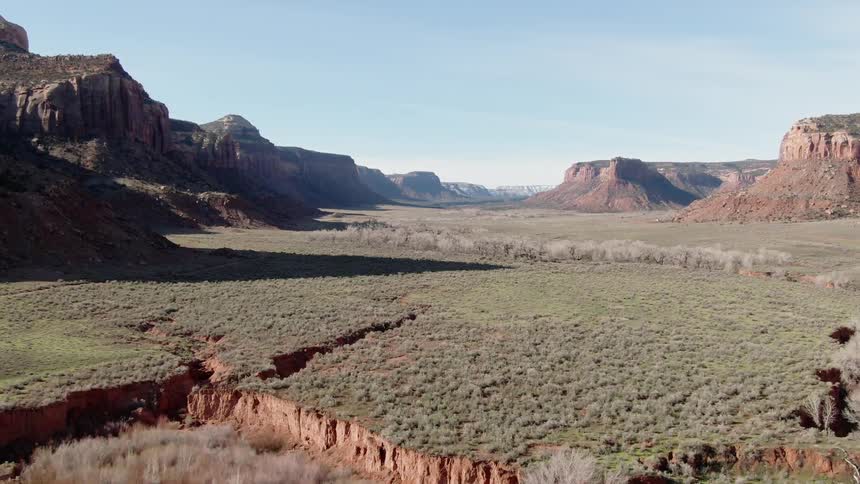 Canyon cliffs are looming over a valley eroded by rivers on a sunny day