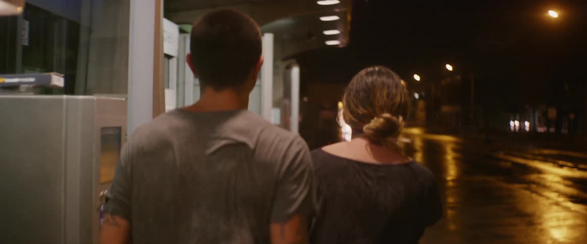 A man and woman walk on a city sidewalk in the rain