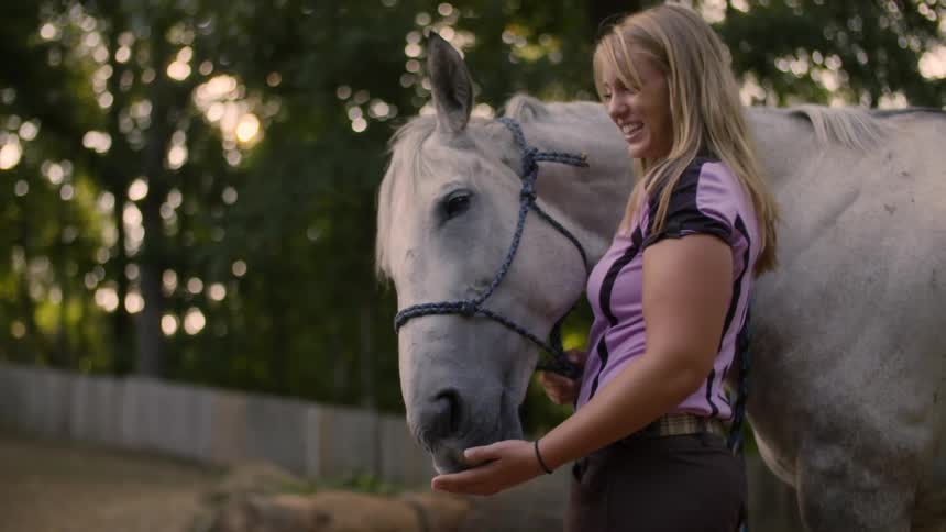 A woman in a pink shirt lets her horse lick her hand