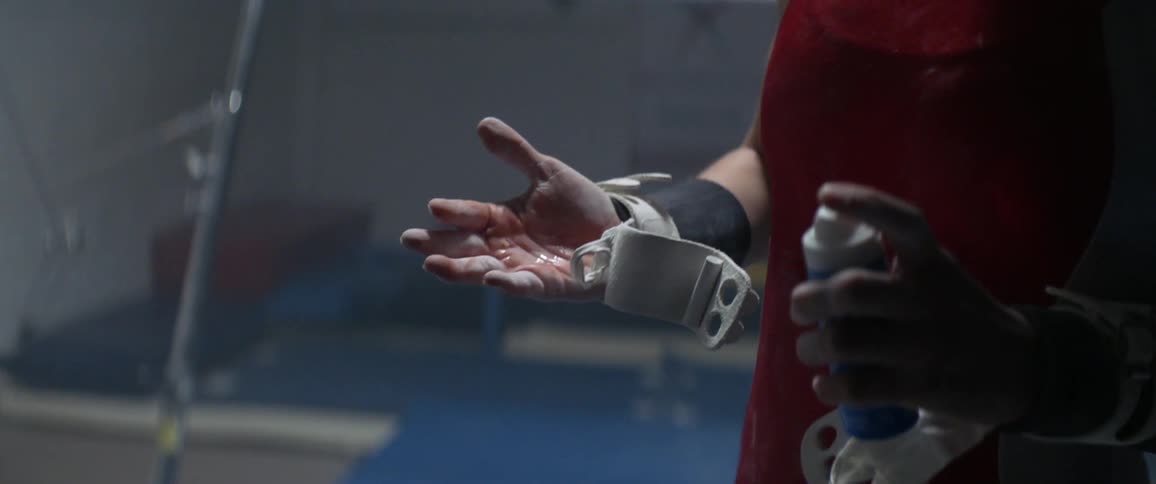 A female gymnast is spraying an ointment onto her hand inside in daylight