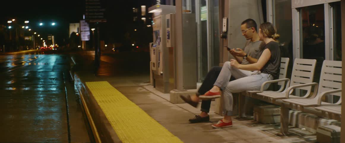Man and woman sit on a bench near a city street