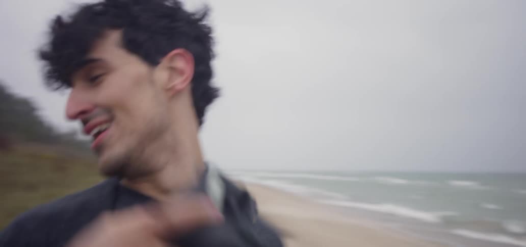 Man takes a photograph of the ocean then turns to run with a woman