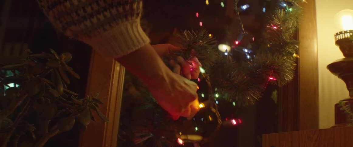 A woman arranges christmas lights around a string of garland inside at night