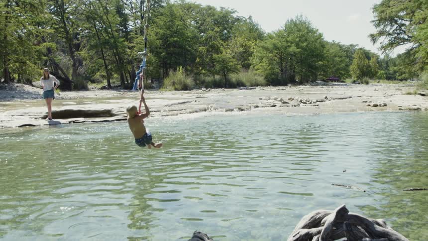 A young boy swings from a rope into the river