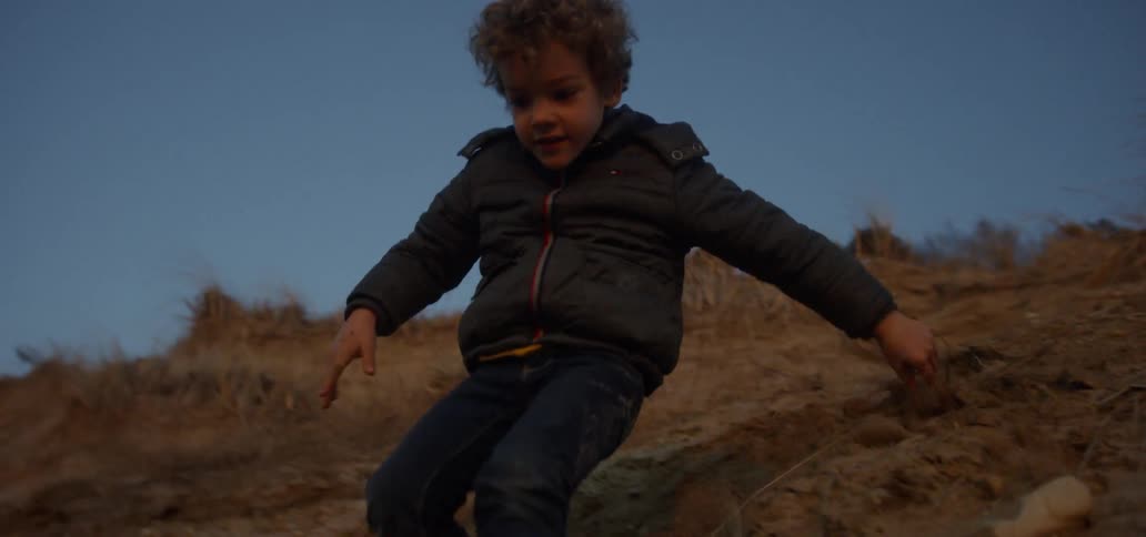 A boy slides down a sandy hillside on a beach at sunset