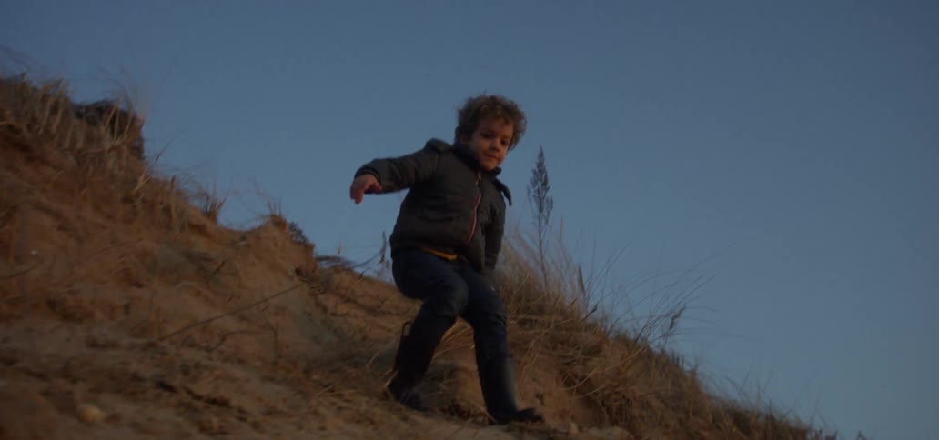 A boy slides and jumps down a sandy slope
