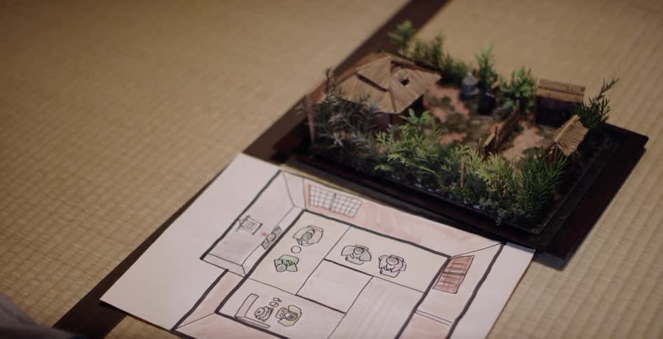 A model of a home sits on a table next to a blueprint drawn on paper
