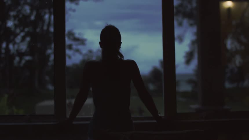Woman looks out a window at sunset