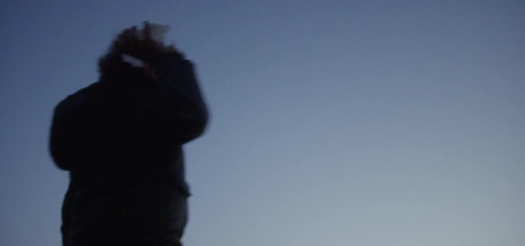 A boy throws sand into the ocean at sunset