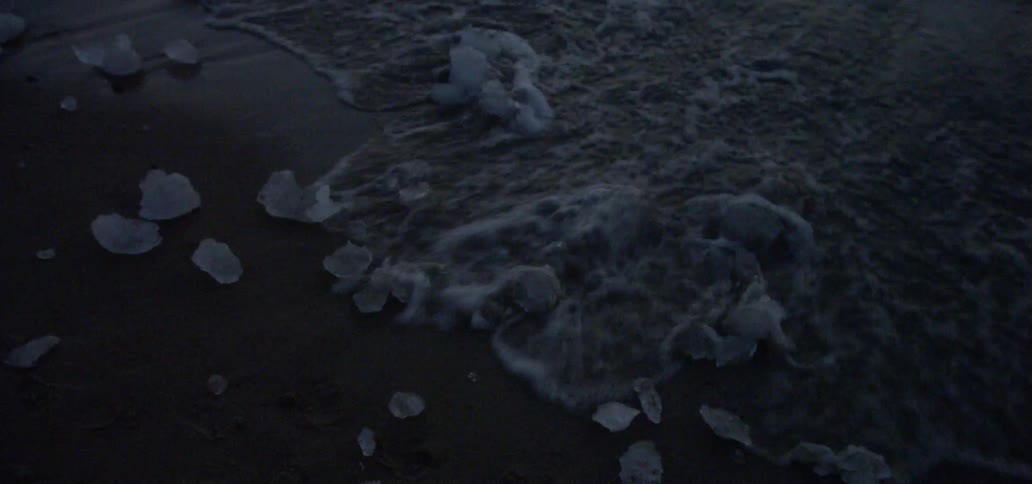 Waves flow around chunks of ice on a beach